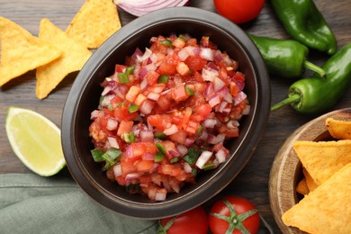 Photo of Delicious salsa in bowl, nacho chips and ingredients on wooden table, flat lay