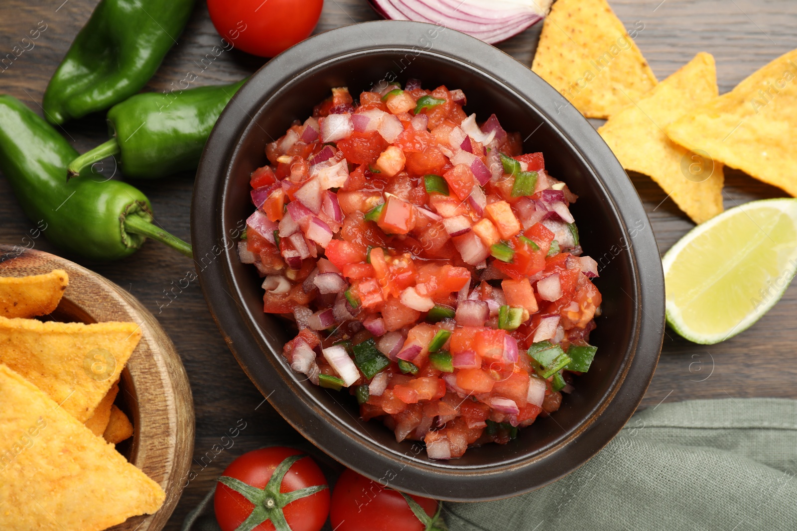 Photo of Delicious salsa in bowl, nacho chips and ingredients on wooden table, flat lay