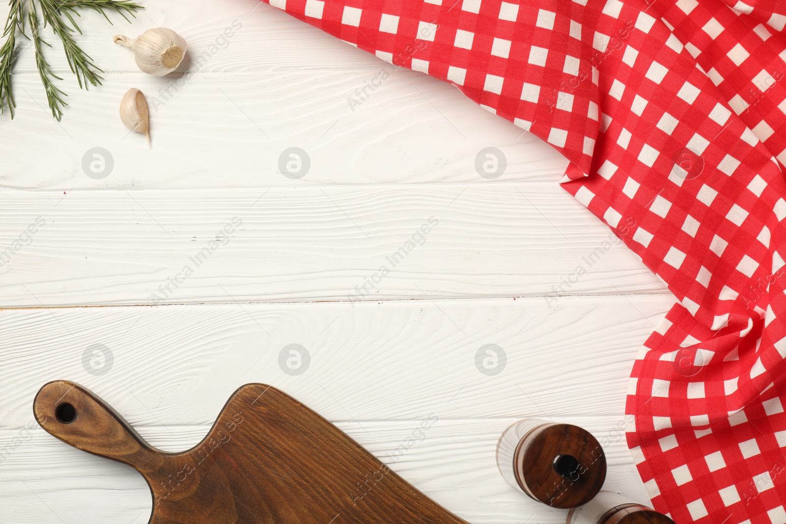 Photo of Checkered tablecloth, cutting board, spices and rosemary on white wooden table, flat lay. Space for text