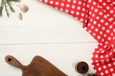 Photo of Checkered tablecloth, cutting board, spices and rosemary on white wooden table, flat lay. Space for text