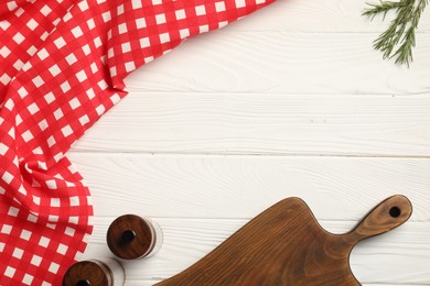 Photo of Checkered tablecloth, cutting board, spices and rosemary on white wooden table, flat lay. Space for text