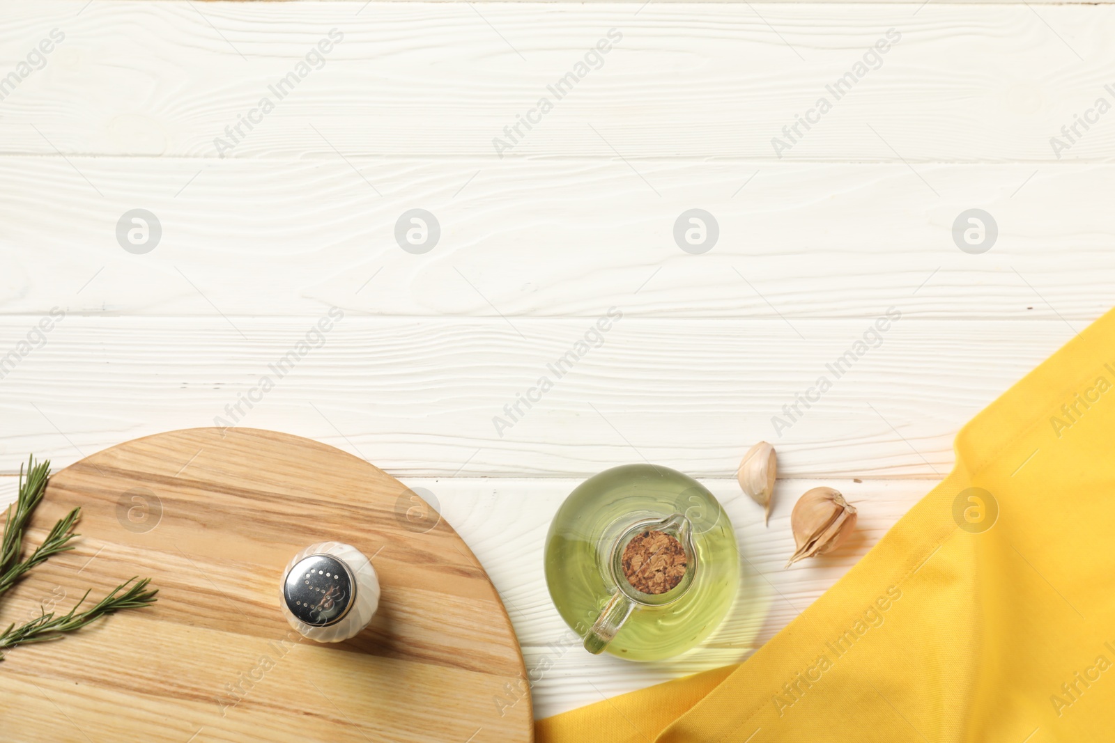 Photo of Yellow tablecloth, cutting board, oil and spices on white wooden table, flat lay. Space for text