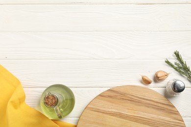 Photo of Yellow tablecloth, cutting board, oil and spices on white wooden table, flat lay. Space for text