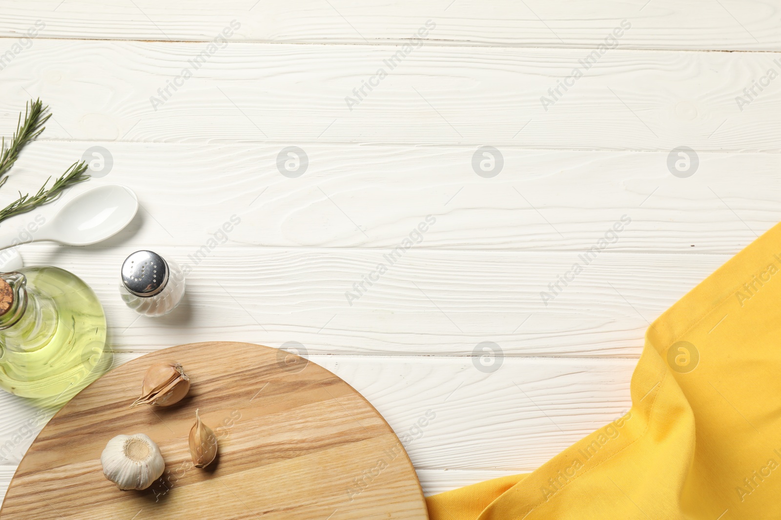 Photo of Yellow tablecloth, cutting board, oil and spices on white wooden table, flat lay. Space for text