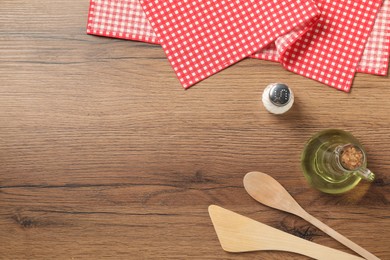 Photo of Checkered tablecloth, cooking utensils, oil and salt on wooden table, flat lay. Space for text