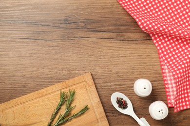 Photo of Checkered tablecloth, cutting board, rosemary and spices on wooden table, flat lay. Space for text