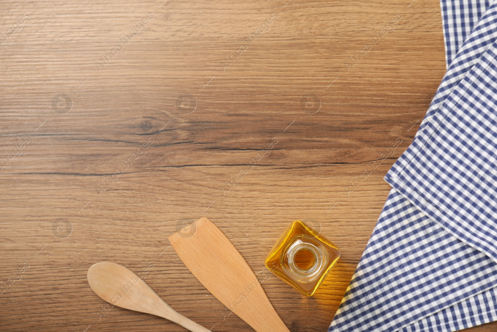 Photo of Checkered tablecloth, cooking utensils and oil on wooden table, flat lay. Space for text