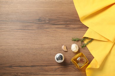 Photo of Yellow tablecloth, oil, rosemary and spices on wooden table, flat lay. Space for text