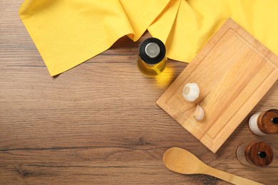 Photo of Yellow tablecloth, cooking utensils, oil and spices on wooden table, flat lay. Space for text