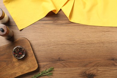 Photo of Yellow tablecloth, rosemary and spices on wooden table, flat lay. Space for text