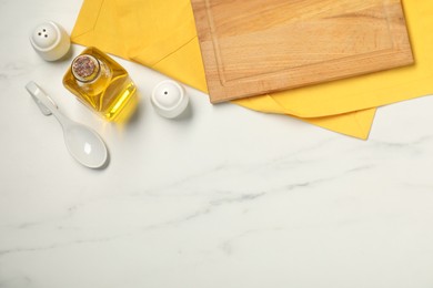 Photo of Yellow tablecloth, cutting board, oil and spices on white marble table, flat lay. Space for text