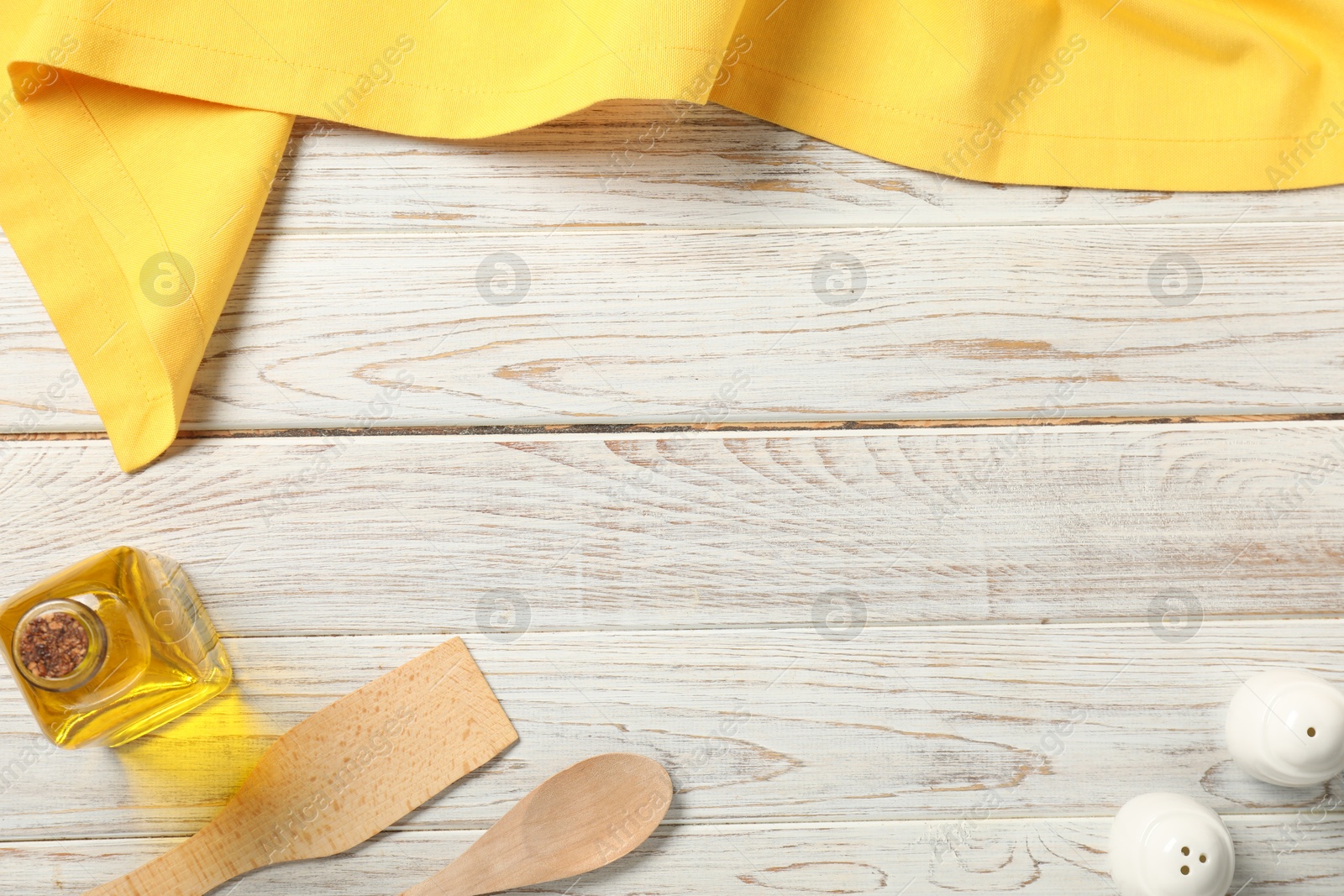 Photo of Yellow tablecloth, cooking utensils, oil and spices on white wooden table, flat lay. Space for text