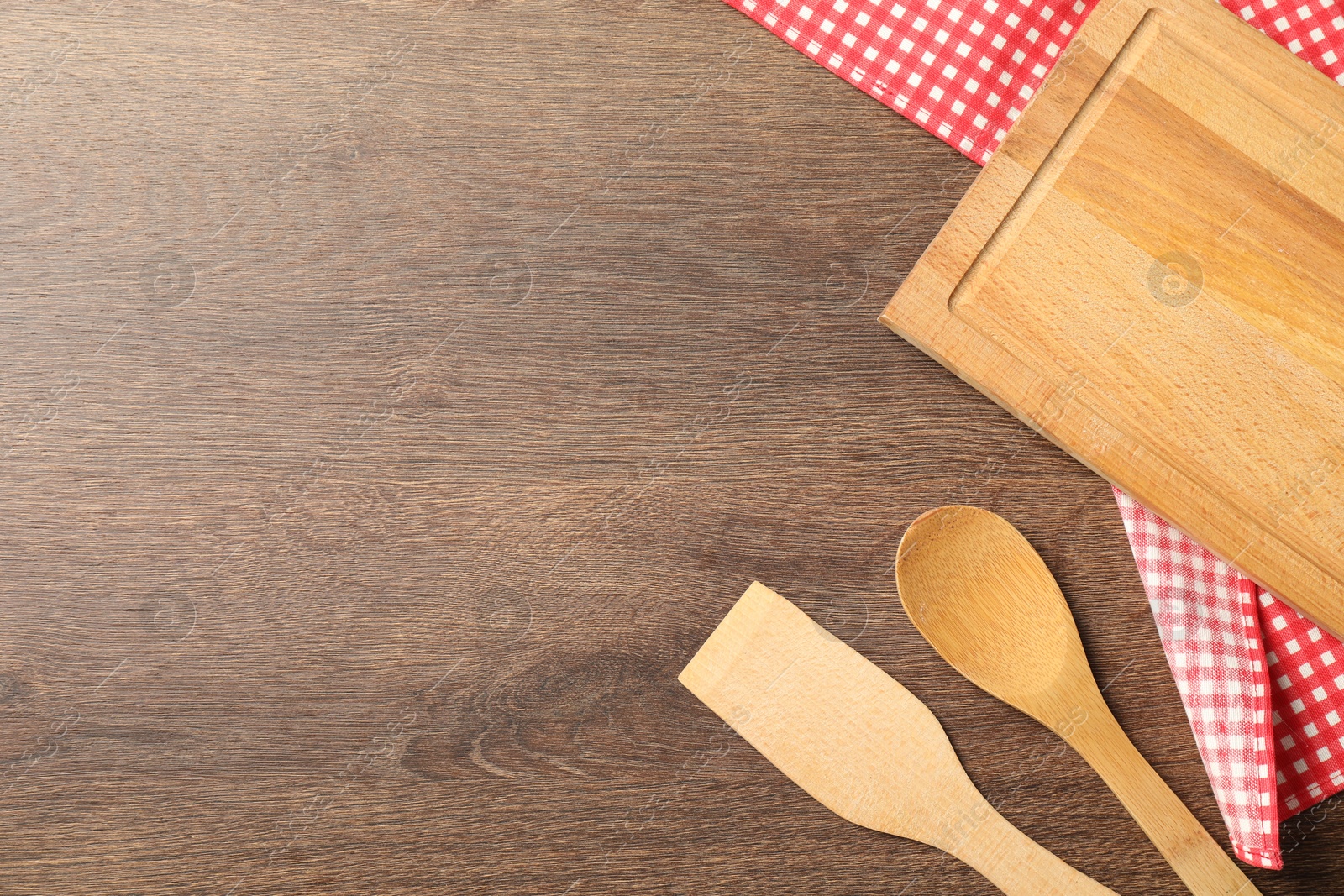 Photo of Checkered tablecloth and cooking utensils on wooden table, flat lay. Space for text