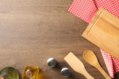 Photo of Checkered tablecloth, cooking utensils, oil and spices on wooden table, flat lay. Space for text