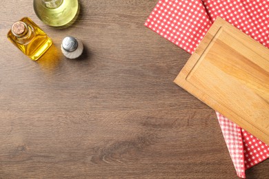 Photo of Checkered tablecloth, cutting board, oil and spice on wooden table, flat lay. Space for text