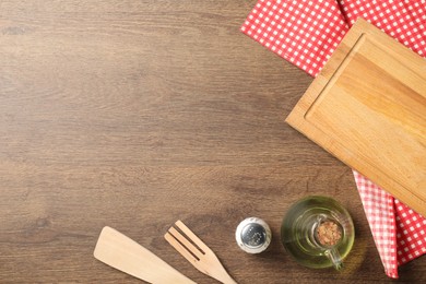 Photo of Checkered tablecloth, cooking utensils, oil and spice on wooden table, flat lay. Space for text