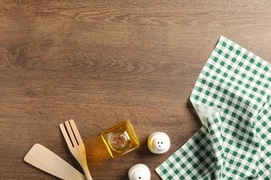 Photo of Checkered tablecloth, cooking utensils, oil and spices on wooden table, flat lay. Space for text