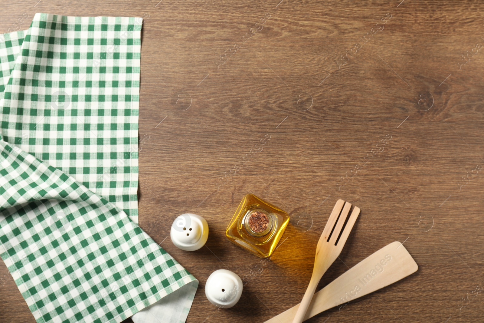 Photo of Checkered tablecloth, cooking utensils, oil and spices on wooden table, flat lay. Space for text