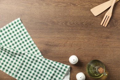 Photo of Checkered tablecloth, cooking utensils, oil and spices on wooden table, flat lay. Space for text