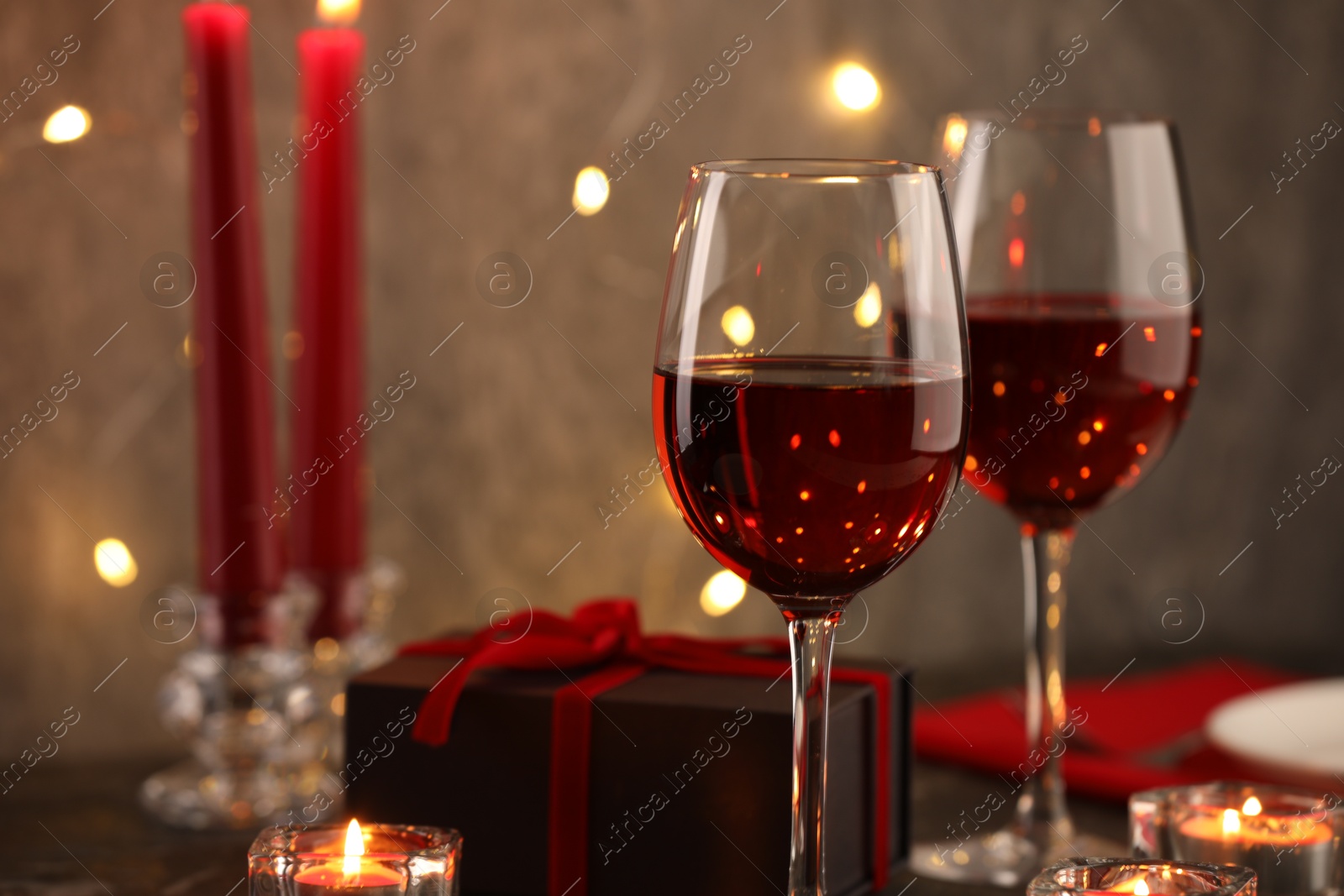 Photo of Glasses of wine, burning candles and gift box on table, closeup. Romantic dinner