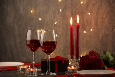 Photo of Glasses of wine, burning candles, gift box and roses on black table. Romantic dinner