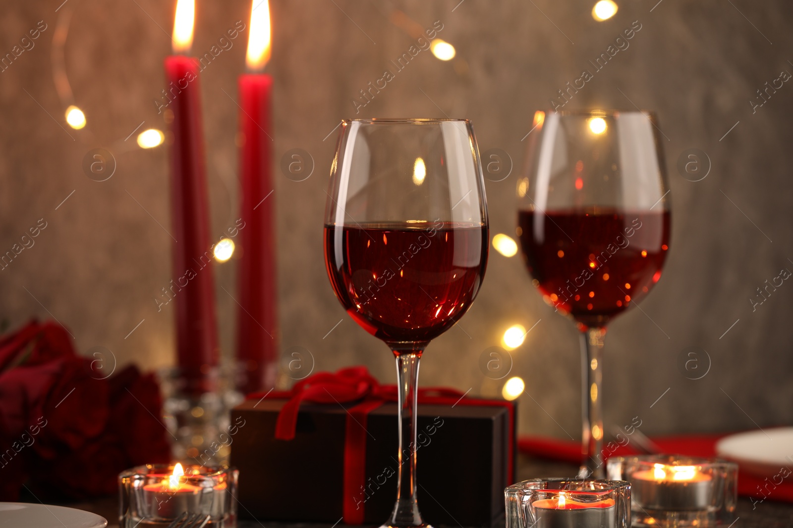 Photo of Glasses of wine, burning candles, gift box and roses on table, closeup. Romantic dinner