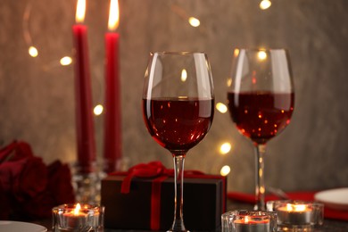 Photo of Glasses of wine, burning candles, gift box and roses on table, closeup. Romantic dinner