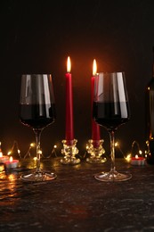 Photo of Glasses of wine and burning candles on black textured table. Romantic dinner