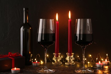 Photo of Glasses of wine, burning candles and gift box on black textured table. Romantic dinner