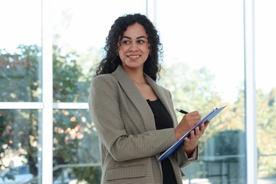 Photo of Portrait of young woman with clipboard wearing stylish suit indoors