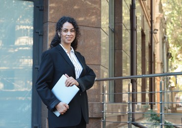 Photo of Portrait of young woman with laptop wearing stylish suit outdoors. Space for text