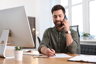 Photo of Man talking on smartphone while working at table in office