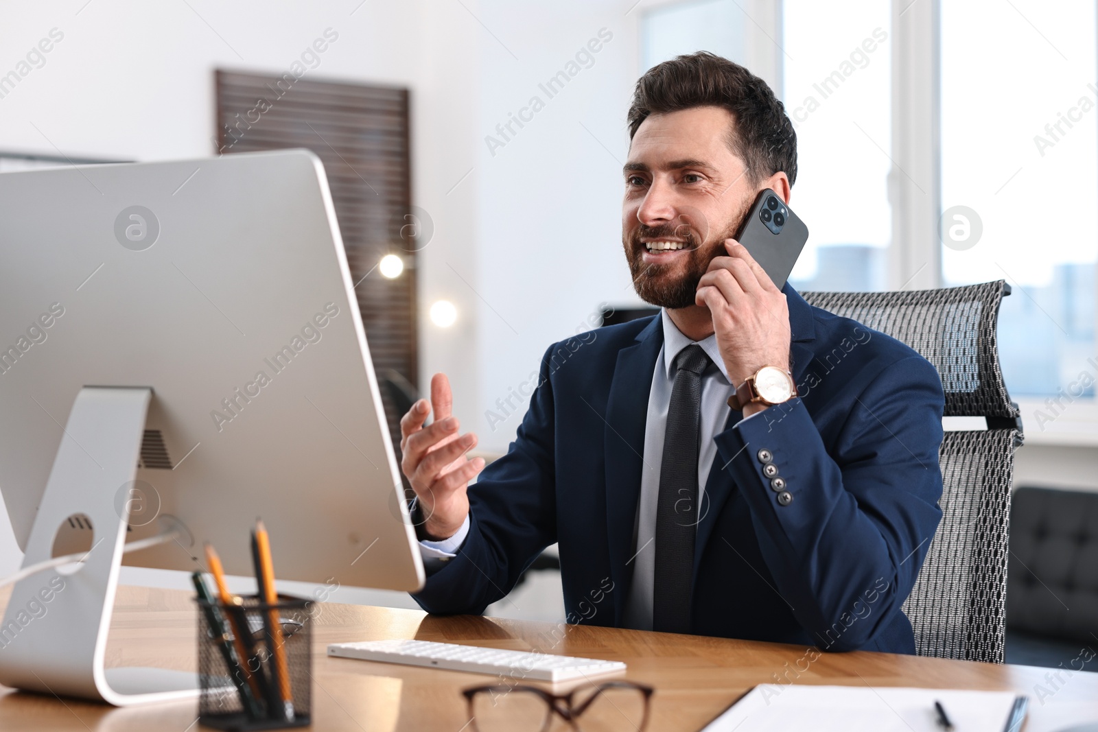 Photo of Man talking on smartphone while working at table in office