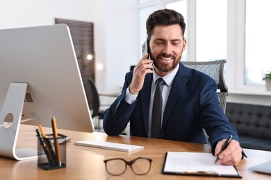 Photo of Man talking on smartphone while working at table in office