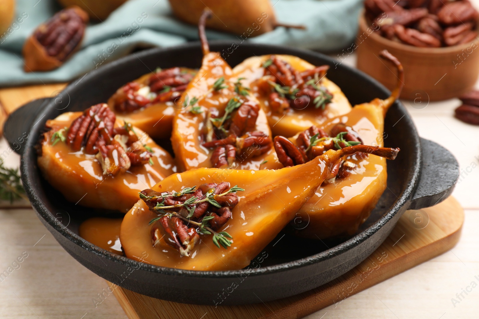 Photo of Delicious pears with caramel sauce, pecan nuts and thyme on wooden table, closeup