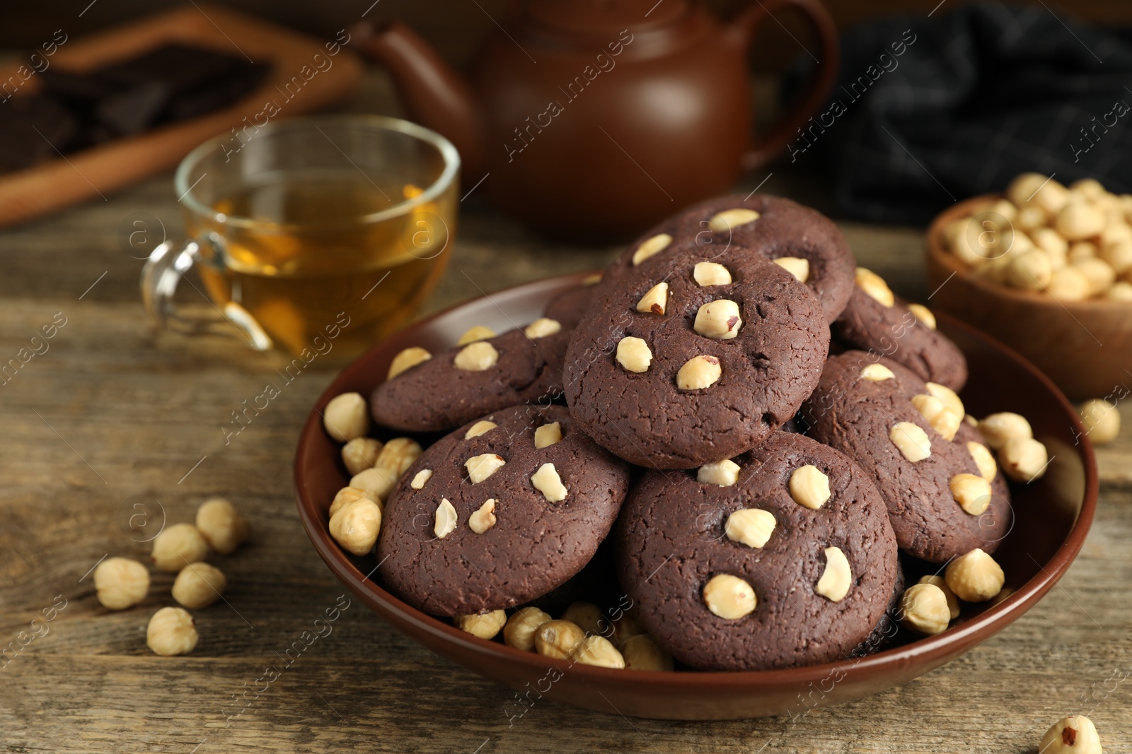 Photo of Tasty chocolate cookies with hazelnuts and tea on wooden table, closeup