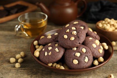 Photo of Tasty chocolate cookies with hazelnuts and tea on wooden table, closeup