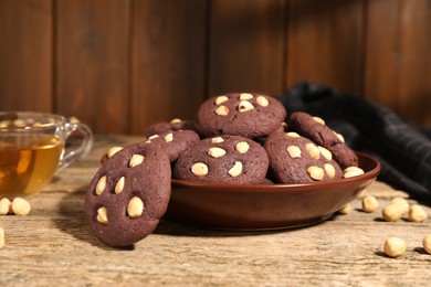 Photo of Tasty chocolate cookies with hazelnuts and tea on wooden table, closeup