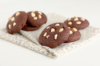 Photo of Tasty chocolate cookies with hazelnuts on white table, closeup