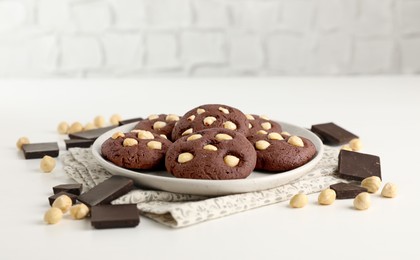 Photo of Tasty chocolate cookies with hazelnuts on white table, closeup