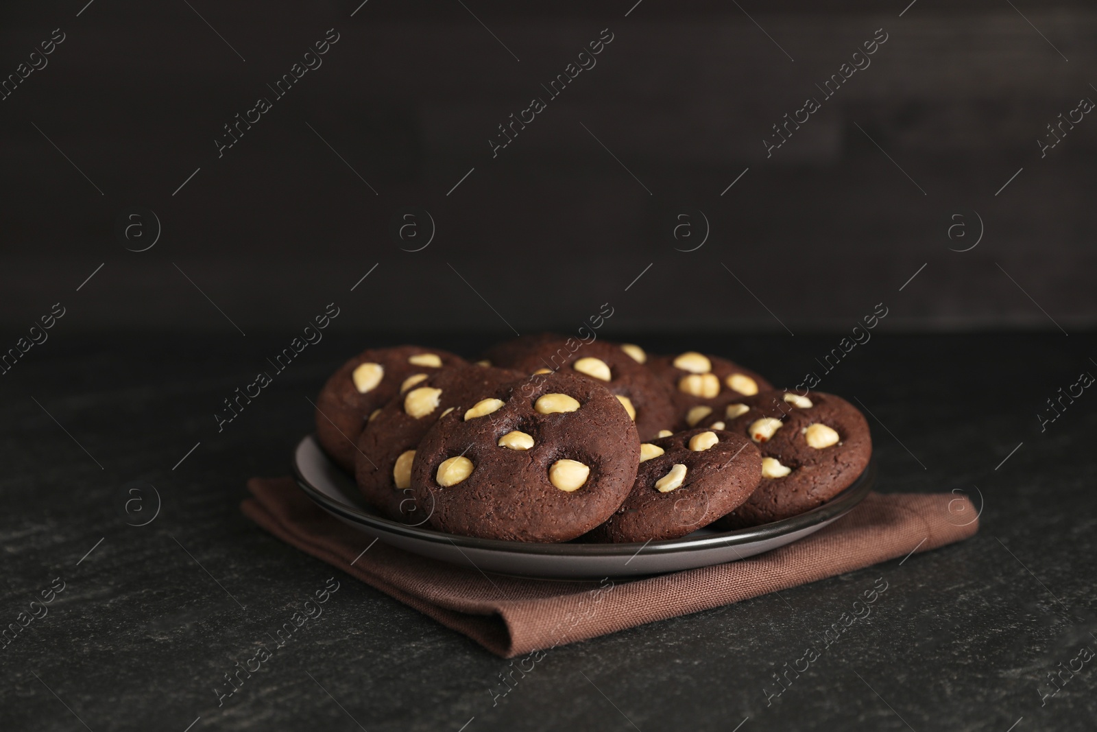 Photo of Tasty chocolate cookies with hazelnuts on black table, closeup