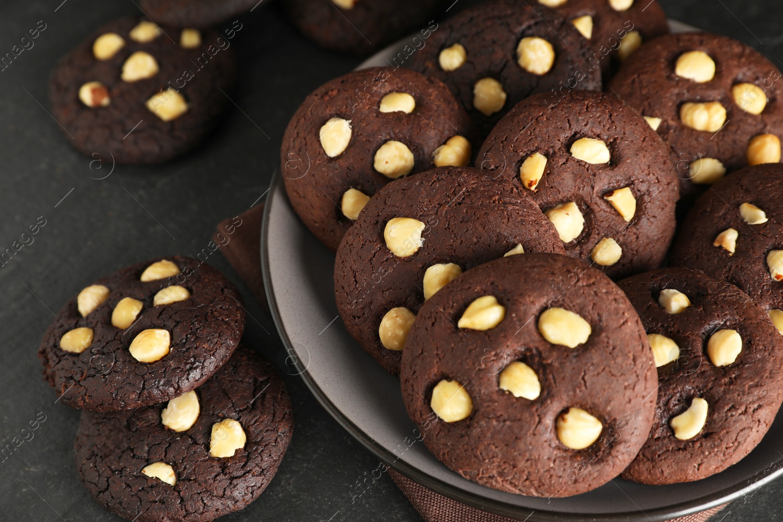 Photo of Tasty chocolate cookies with hazelnuts on black table, closeup