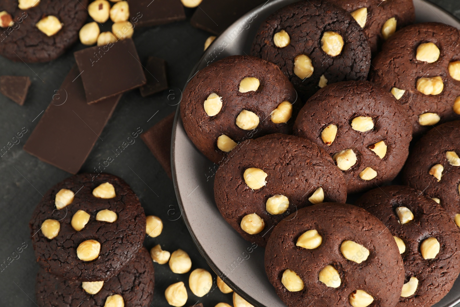 Photo of Tasty chocolate cookies with hazelnuts on black table, flat lay