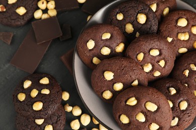 Photo of Tasty chocolate cookies with hazelnuts on black table, flat lay