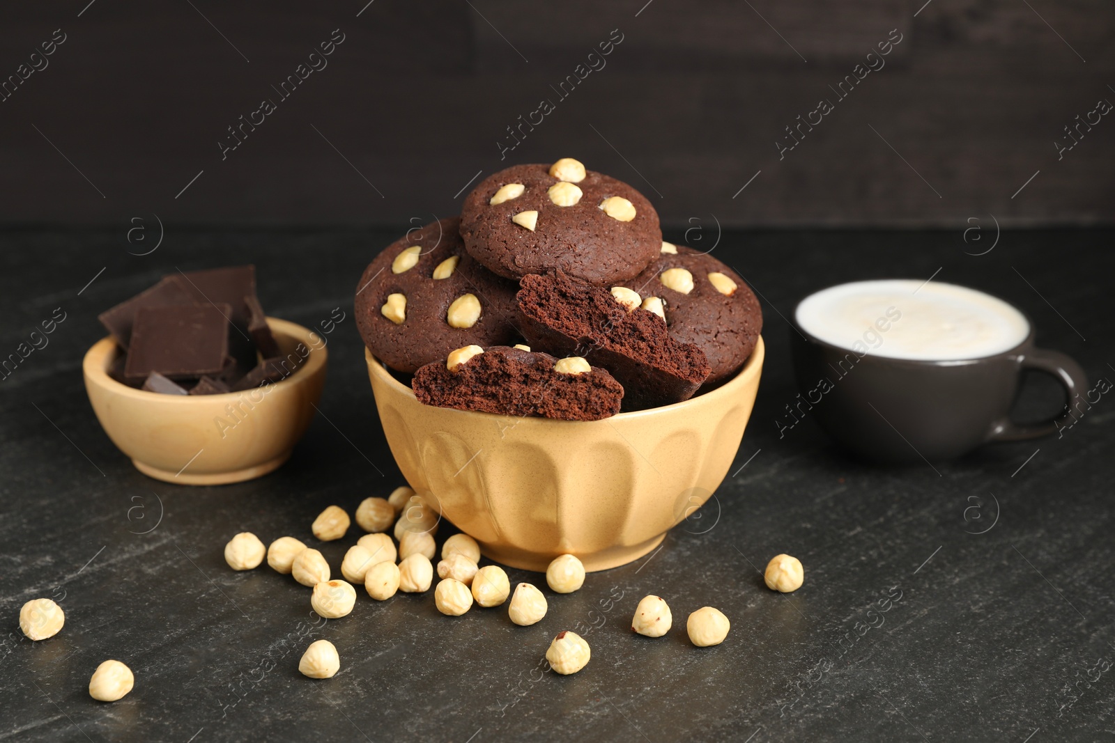 Photo of Tasty chocolate cookies with hazelnuts and coffee on black table