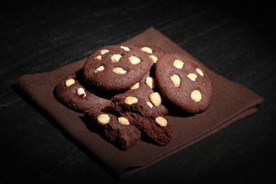 Photo of Tasty chocolate cookies with hazelnuts on black table, closeup