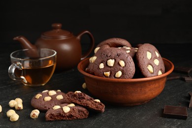 Photo of Tasty chocolate cookies with hazelnuts and tea on black table