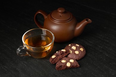 Photo of Tasty chocolate cookies with hazelnuts and tea on black table