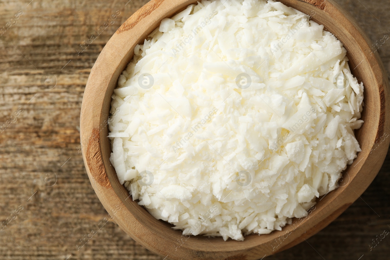 Photo of White soy wax flakes in bowl on wooden table, top view