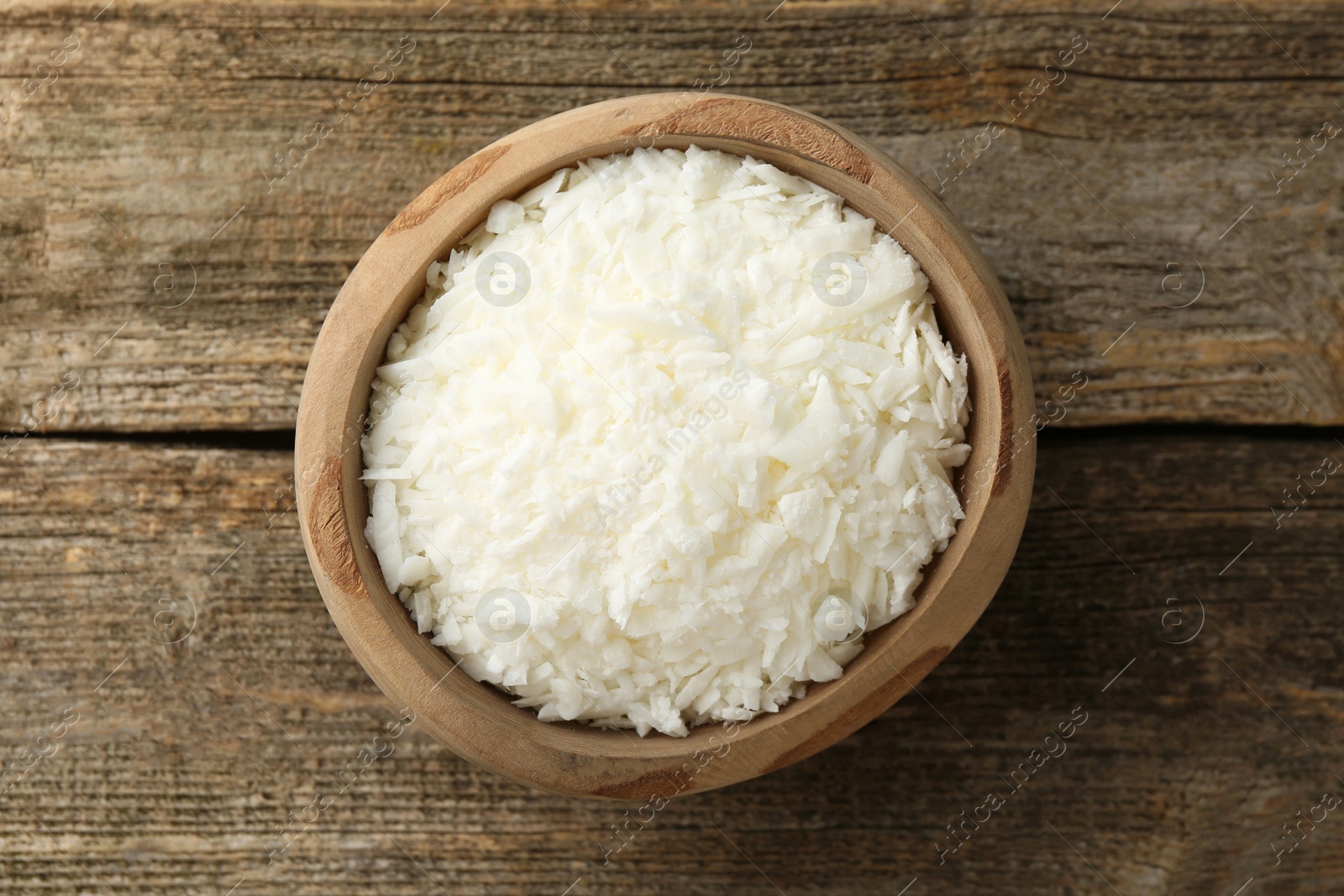 Photo of White soy wax flakes in bowl on wooden table, top view